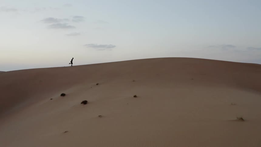A man is running over a sand dune at dusk