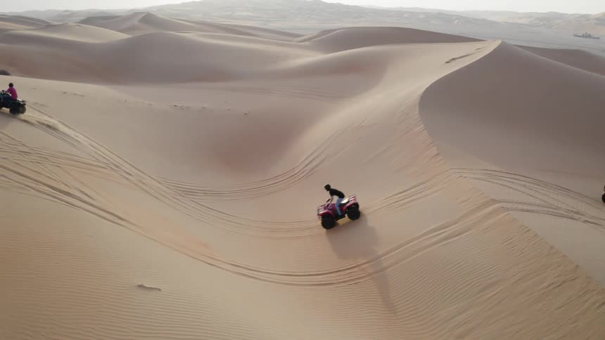 Four wheelers are driven over sand dunes in a desert