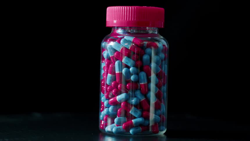 Blue and red capsules in a clear pill bottle