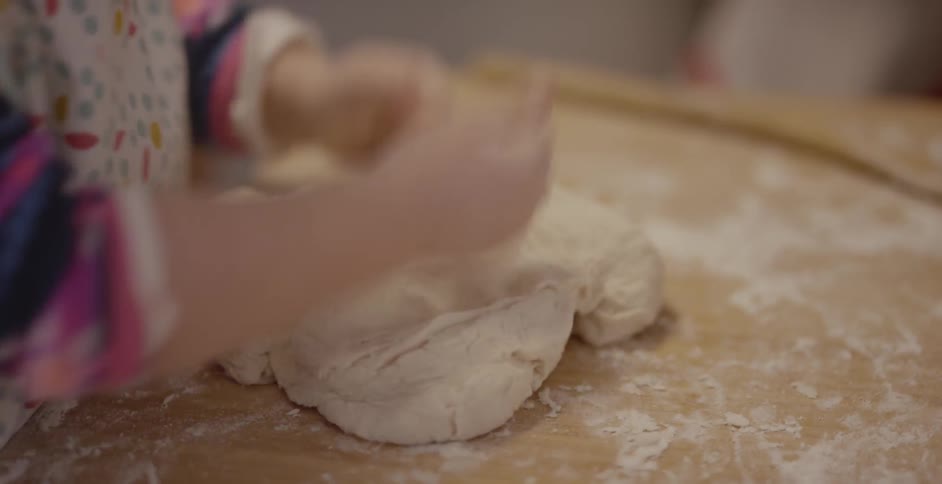 Child pounds dough on a wooden table