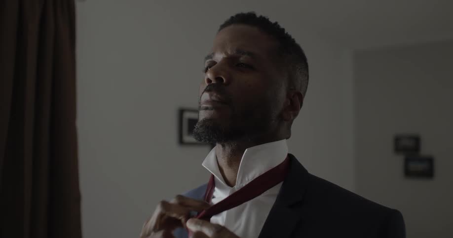 A man in a suit puts on a tie