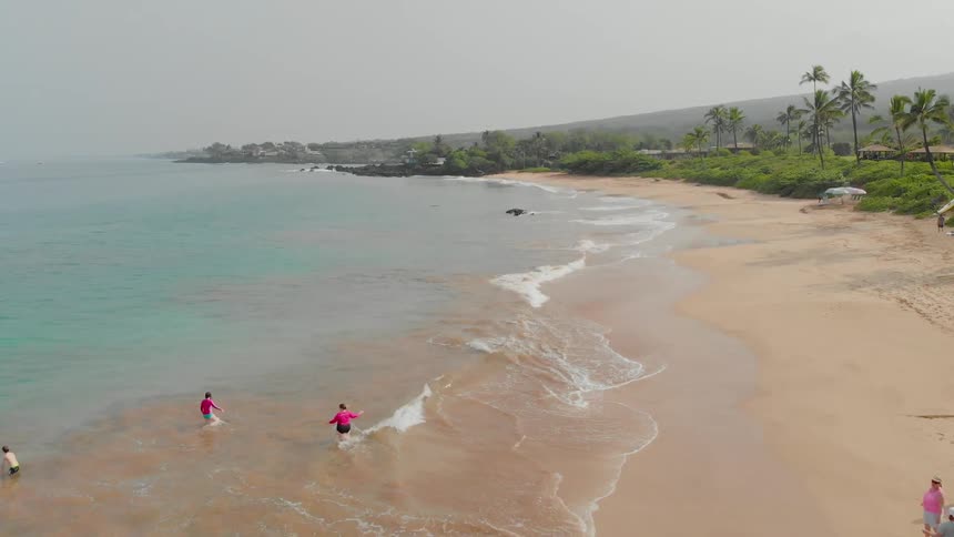 People wade into the surf on the beach