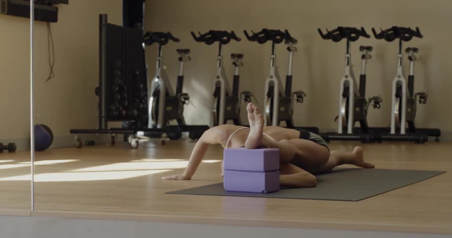 A woman stretches her leg over her head on the mat of a gym