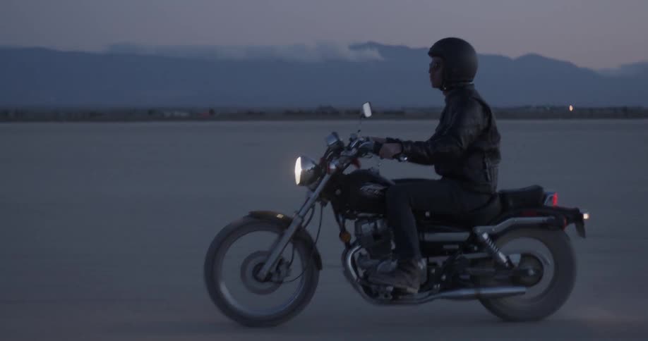 A man rides a motorcycle in the desert at sunset