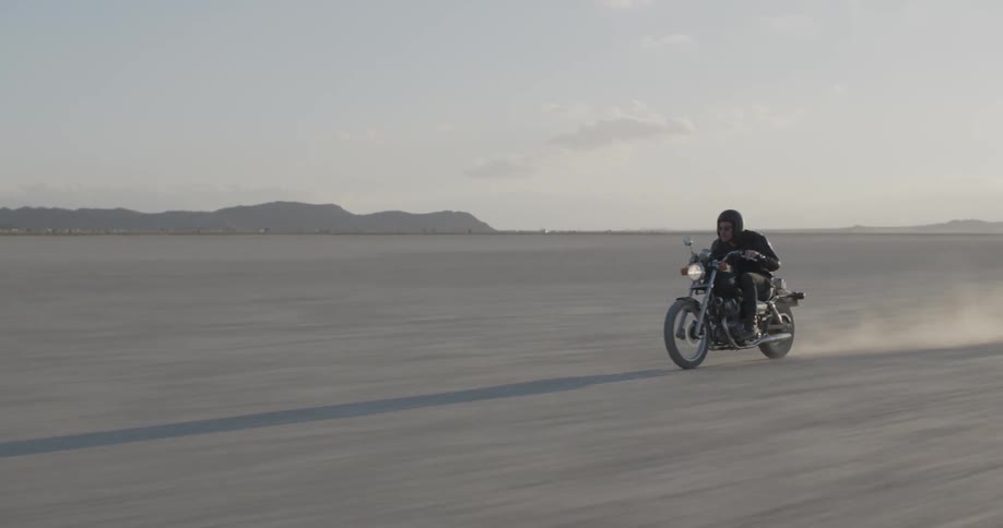 Man riding motorcycle fast through dirt in desolate open flatland