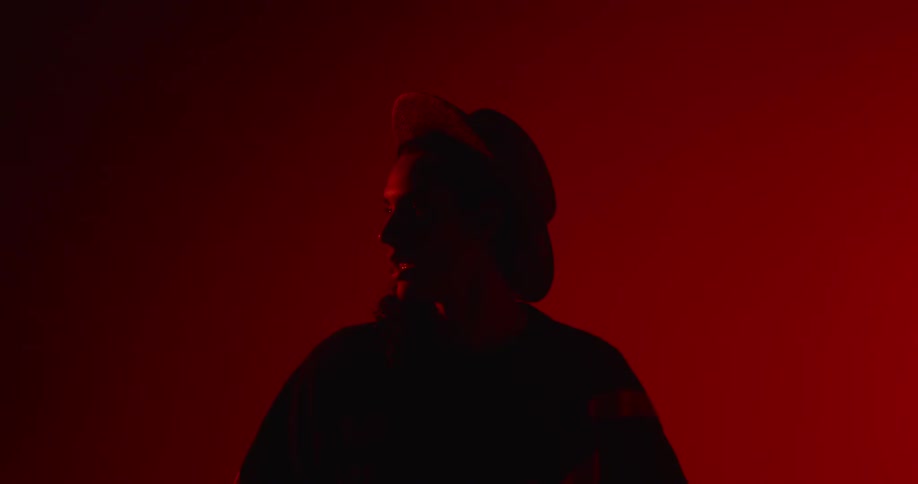 Woman wearing a hat talks in a red lighted room