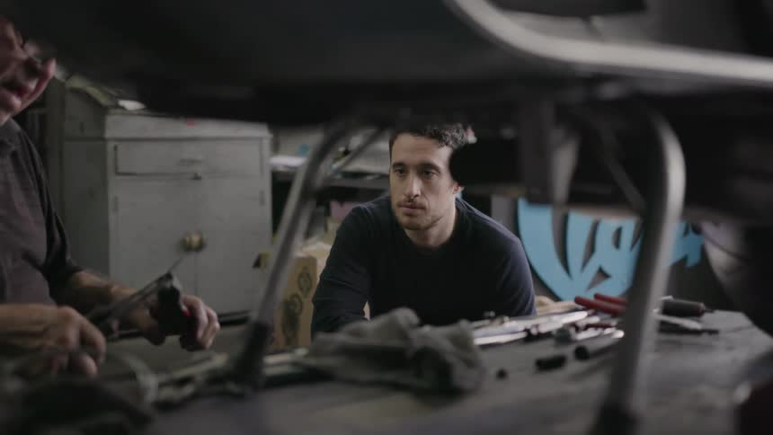 A man watches another man work in a shop