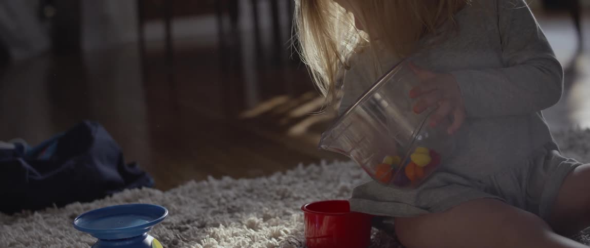 A child sits on a rug and plays with a toy