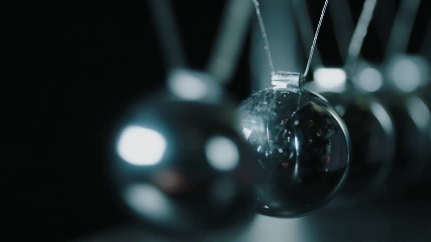 Silver ball suspended from wires bangs against another silver ball