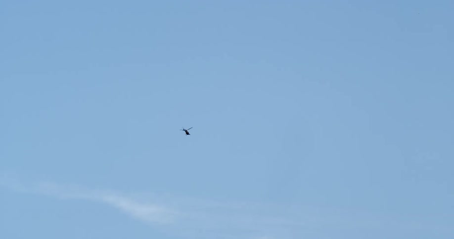 The helicopter flies high in the clear sky