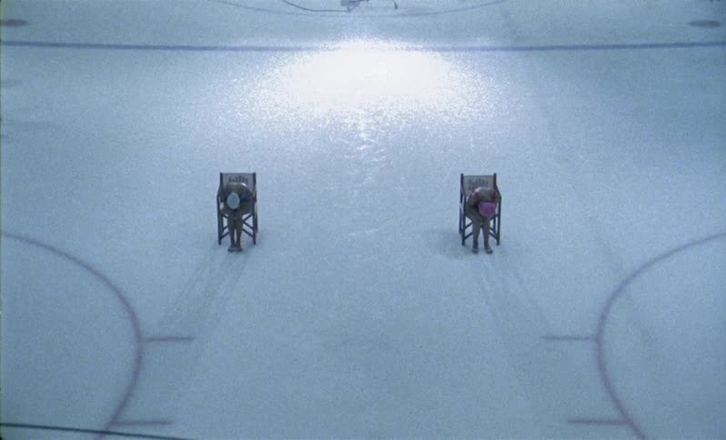Hockey players skate by synchronized swimmers on an ice rink