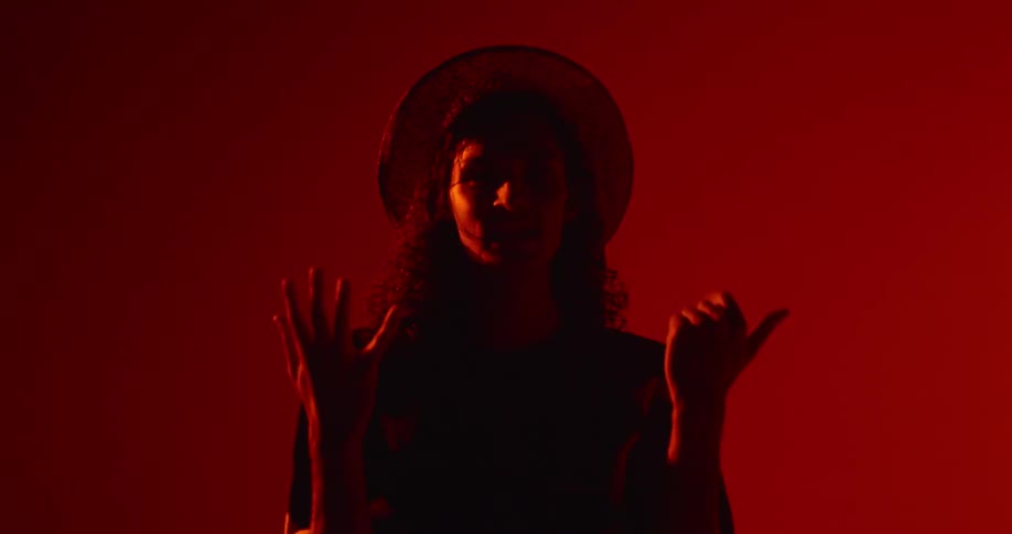 A man is standing in front of a red screen holding up his hands and counting to seven