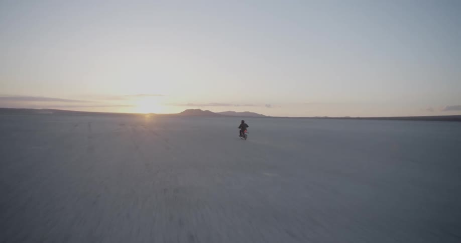 A motorcyclist rides across a desert at sunset