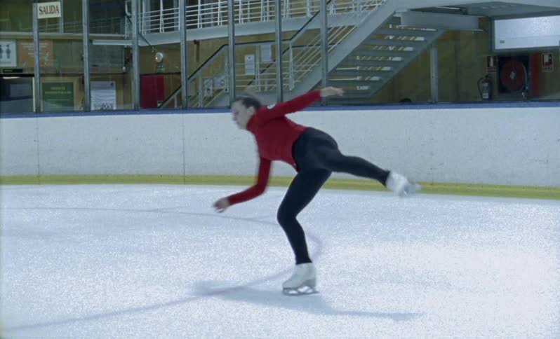 A woman is practicing an ice skating routine inside in daylight