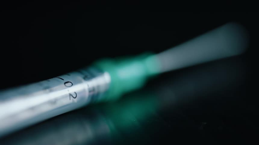 An empty hypodermic needle is sitting on a reflective surface