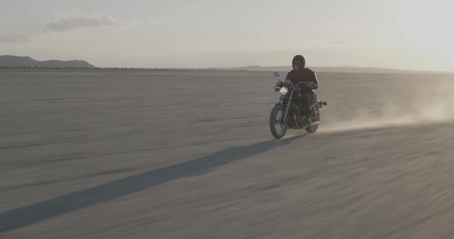 Person rides motorbike across flat desert at sunset