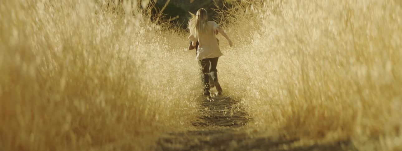 A man and woman run through a grassy field