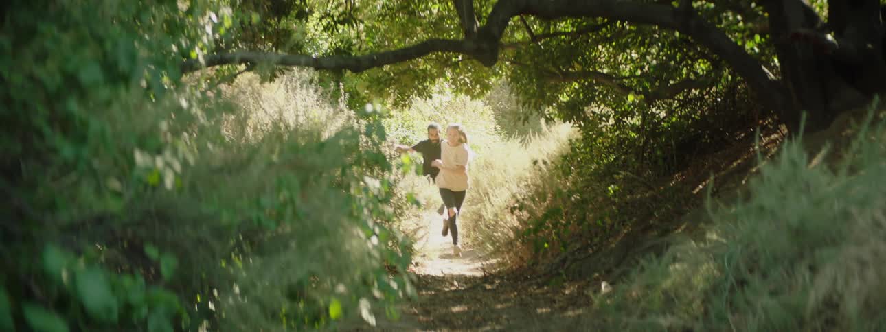 A man and woman run on a trail through tall grass and trees