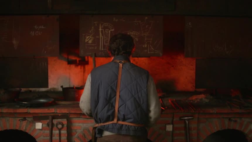 An artisan is working at a forge inside a workshop in daylight