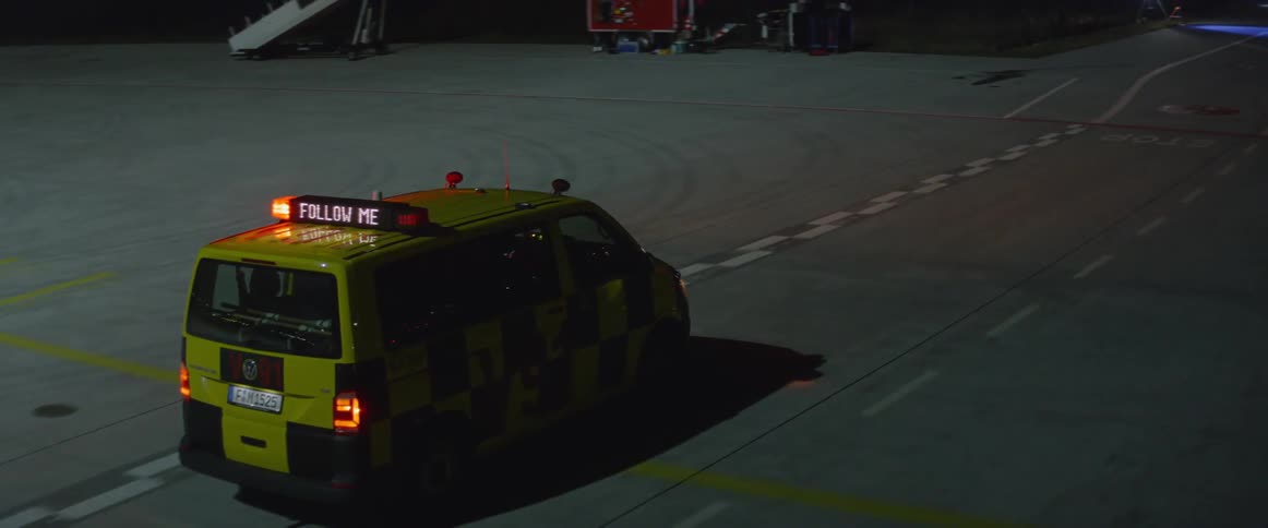 A van with flashing lights is driving at an airport at night