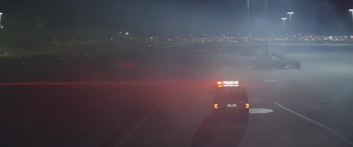 A van with flashing lights drives at a foggy airport