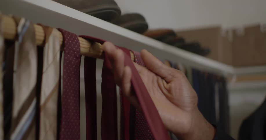 A man selects a necktie from a rack in a closet