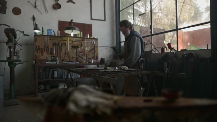 A man is approaching a workbench in a metal working shop in daylight