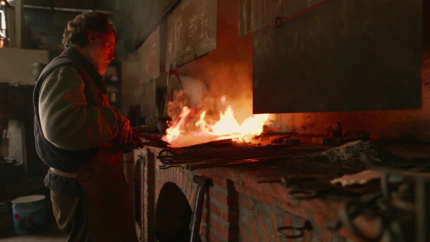 A man is heating a sheet of metal on a forge inside in daylight