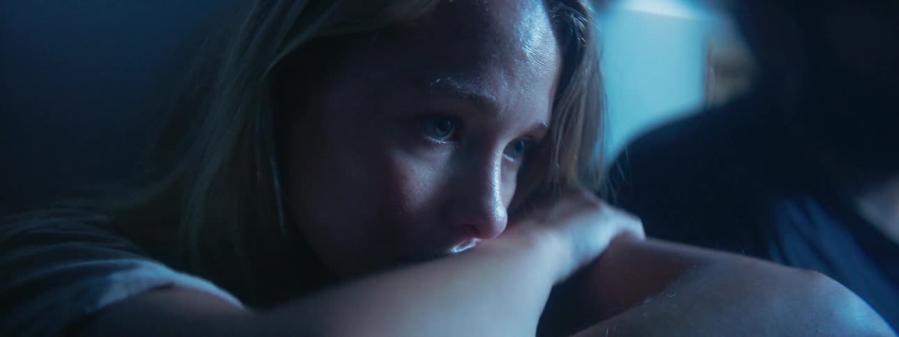 Woman in a dark room looking very sad as a light illuminates her briefly