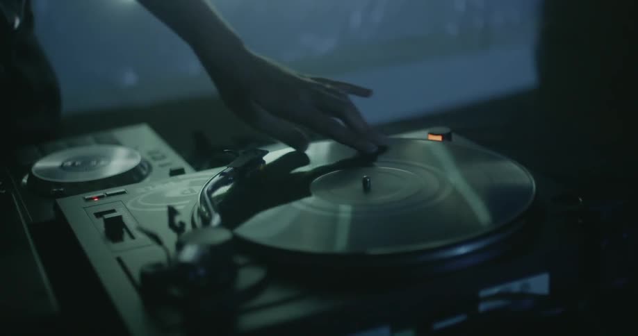 A dj is spinning and stopping a vinyl record on a turntable inside at night