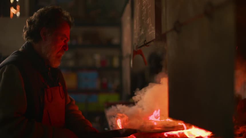 A blacksmith works in front of a fire