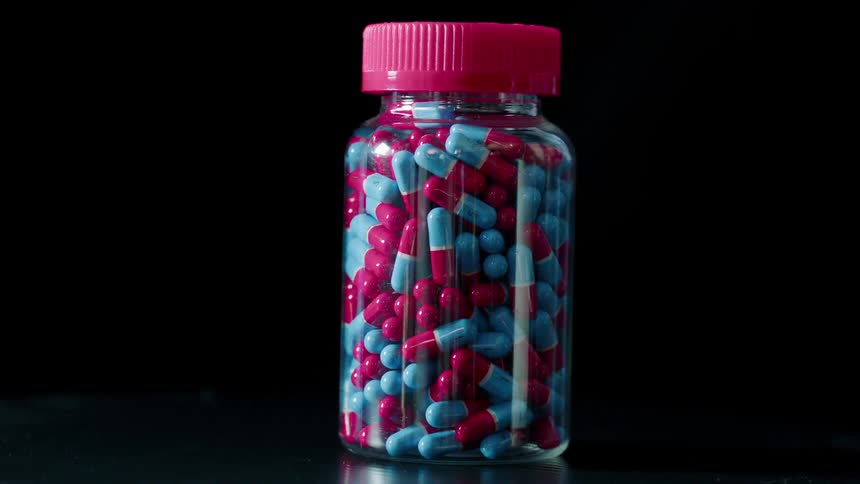 Red and blue pills in a clear jar with a red lid