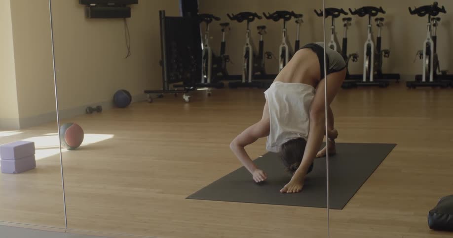 The image of a woman stretching and holding a pose is reflected in a gym mirror