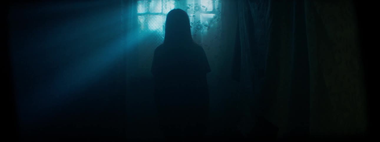 A woman stands in front of a window in a dark room