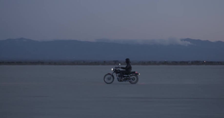 The person races their motorcycle over the flat field
