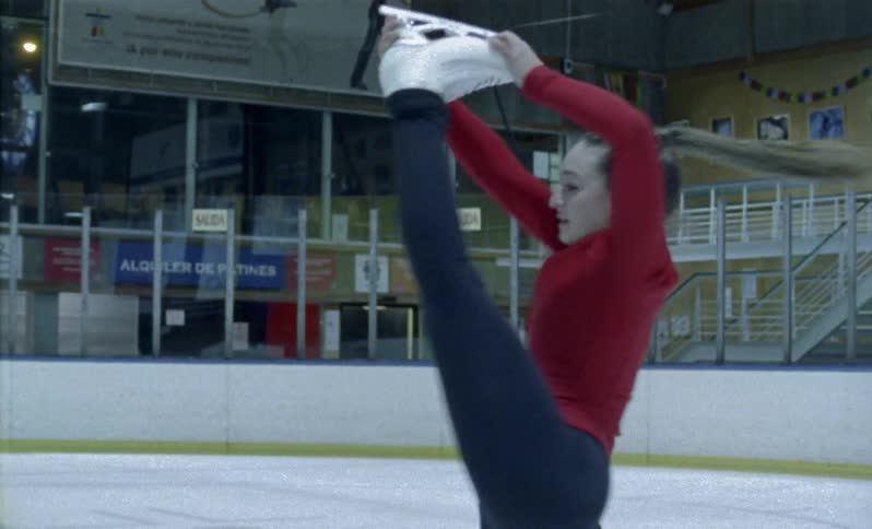 A woman lifts her skate over her head as she twirls on the ice