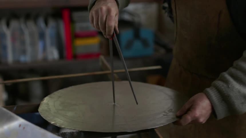 A worker draws a circle on metal with a compass