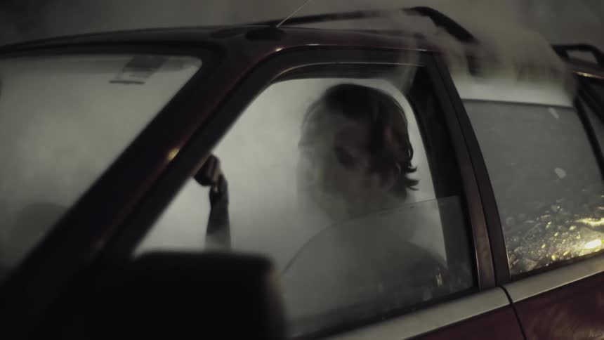 A man sits in a car that is filled with smoke