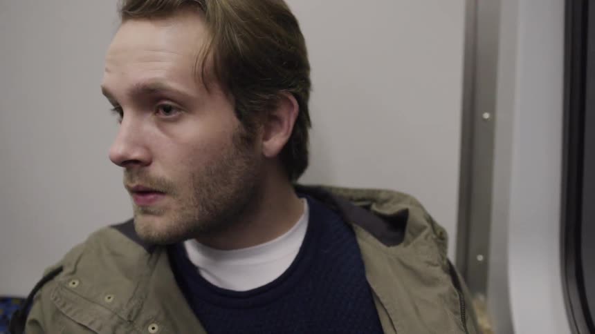 Man with a khaki coat sits on a train and looks around at night