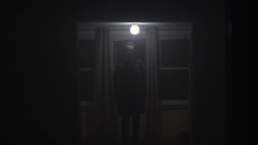 A man standing under a light in front of windows in a dim room