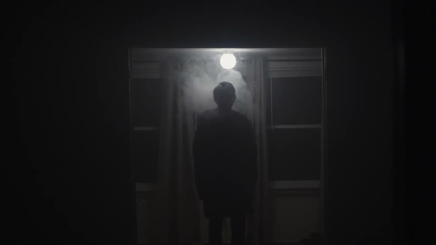 Man standing under a small light with smoke surrounding him
