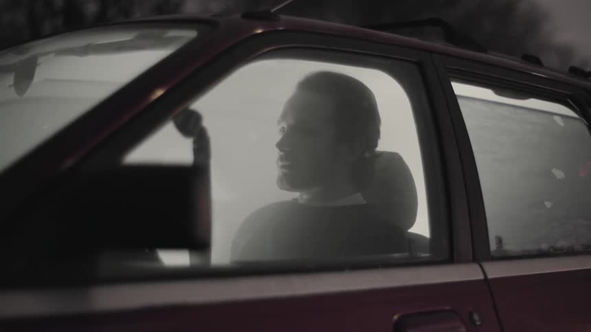 A man sits in a car that is filled with smoke