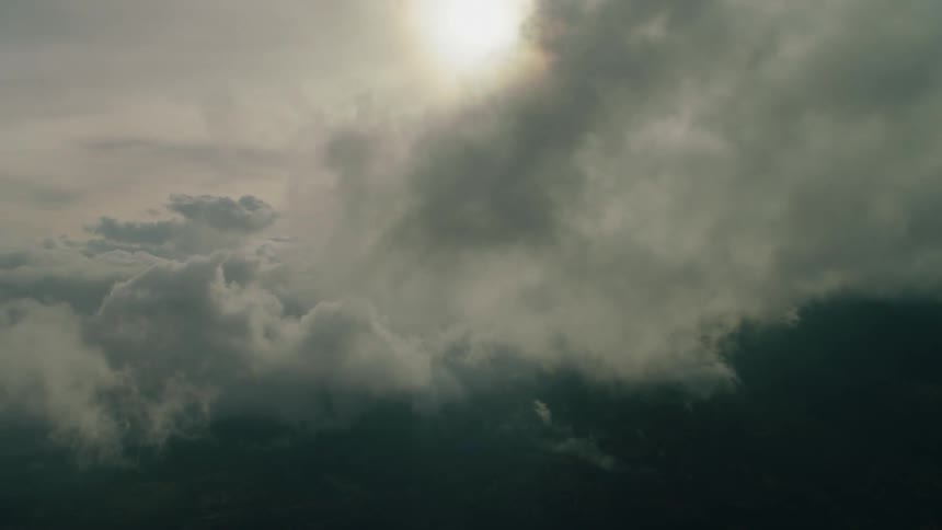 The sun is shining behind drifting clouds over a mountain landscape