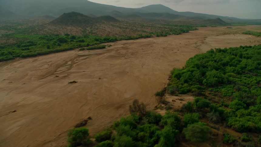 A dry riverbed is winding through a remote landscape in daylight
