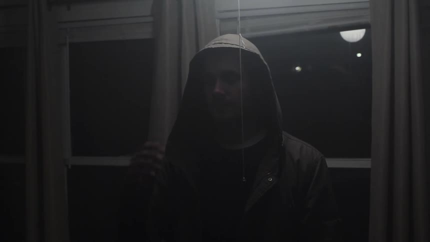 A man in a jacket stands in front of windows at night