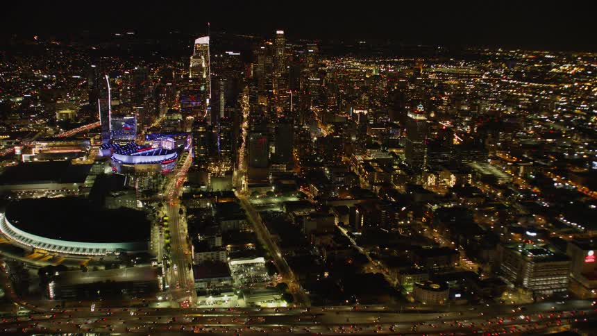 Cars drive on a city highway in front of the LA Skyline; Night