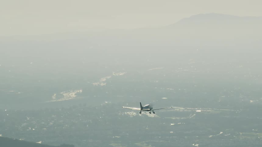 Small airplane flies over a town near hills