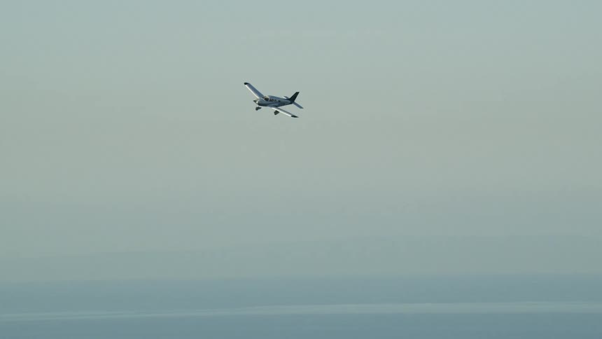 Small airplane flies over a large body of water on a cloudy day