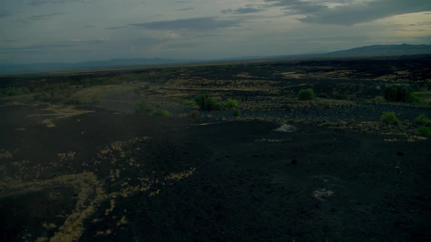 Sun shines behind clouds over grassy muddy flat land