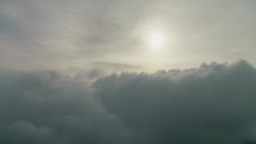 The sun is shining on clouds as they drift over a mountain range